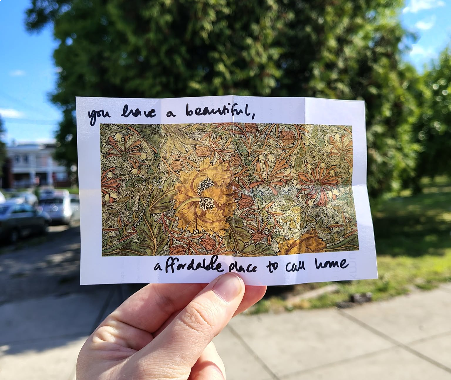A hand holding up a folded piece of paper that says "You have a beautiful, affordable, place to call home"